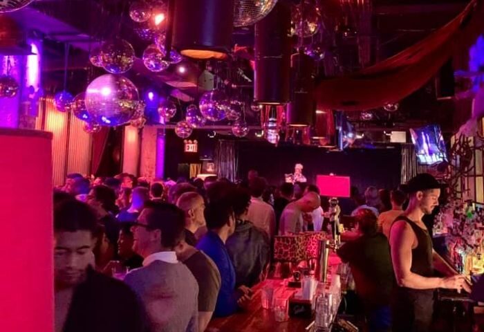 Industry Bar in New York: A lively gay bar scene with disco balls, a crowded bar, and a bartender serving drinks. Gay travel advice.