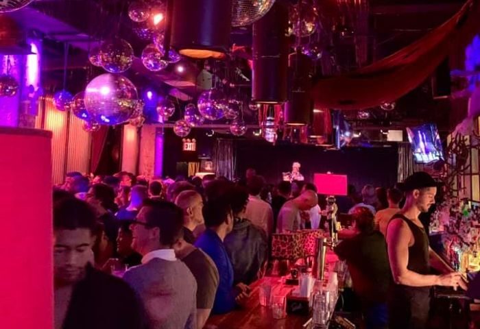 Industry Bar in New York: A lively gay bar scene with disco balls, a crowded bar, and a bartender serving drinks. Gay travel advice.