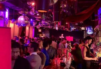 Industry Bar in New York: A lively gay bar scene with disco balls, a crowded bar, and a bartender serving drinks. Gay travel advice.