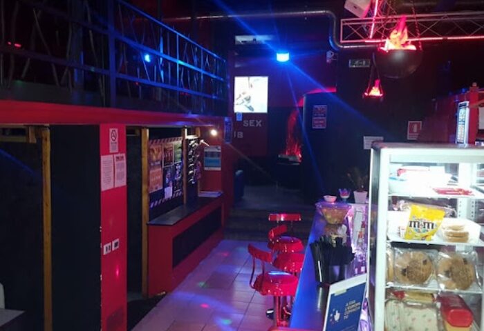 Inferus Club Milan interior. Gay travel advice: Bar area with red stools, snacks, and colorful lighting. Nightlife scene.