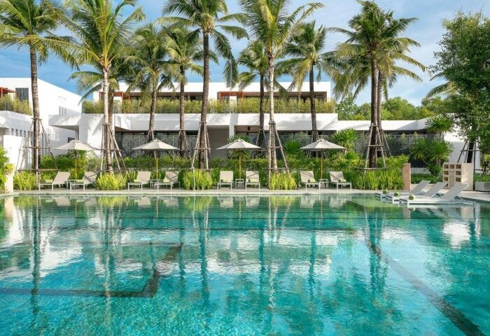 Melia Phuket Mai Khao gay-friendly luxury resort pool view. Palm trees, sunbeds, and umbrellas reflecting in the turquoise water. Thailand travel.