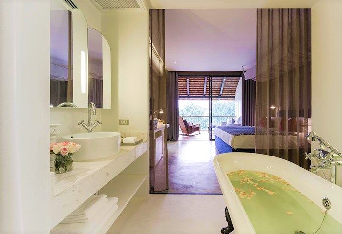 Sala Lanna Chiang Mai LGBT-friendly hotel room. Bathtub with flower petals, sink, and a view to the bedroom and balcony. Gay travel.
