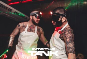 Into the Tank Gay Club Madrid: Two tattooed men in aprons and futuristic eyewear at a party. Nightlife scene.