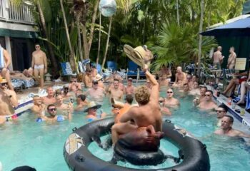 Gay cruising in Key West at Island House: shirtless men enjoying a pool party with drinks, hats, and tropical vibes. Gay travel.