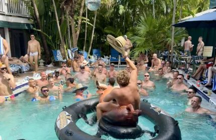 Gay cruising in Key West at Island House: shirtless men enjoying a pool party with drinks, hats, and tropical vibes. Gay travel.