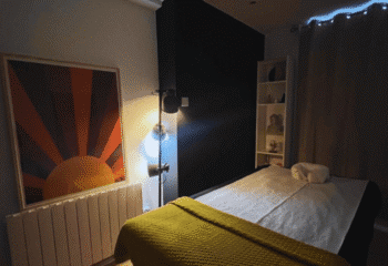 Gay spa massage room in Dublin. Massage table with yellow blanket, sun art, black wall, and shelf. It's Always Sunny, a gay travel tip.