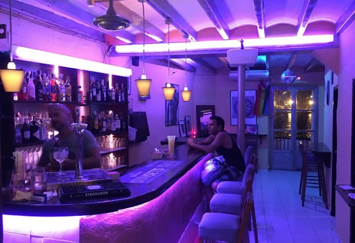 JJ Bar, a gay bar in Ibiza. Drinks are served under purple lights. A man sits at the bar in this popular gay travel destination.