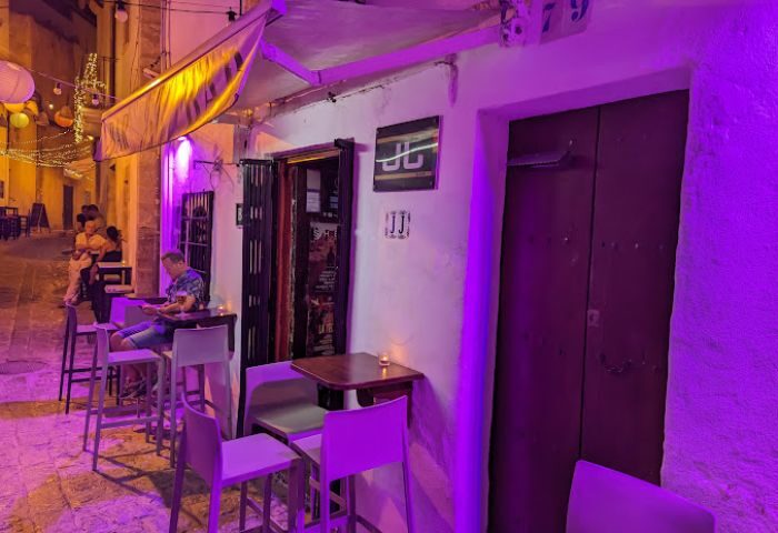 JJ Bar, a gay bar in Ibiza. Outdoor seating, purple lighting, and people enjoying drinks. Gay travel destination.