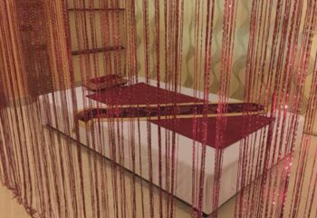 Jack Spa Ho Chi Minh: Massage bed with red accents, seen through a beaded curtain. Gay travel spa experience in Vietnam.