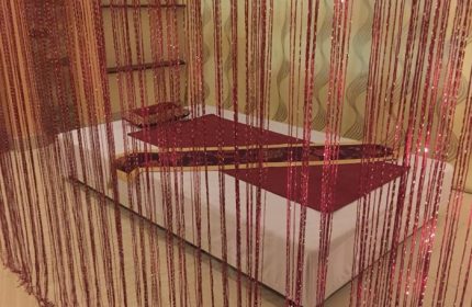 Jack Spa Ho Chi Minh: Massage bed with red accents, seen through a beaded curtain. Gay travel spa experience in Vietnam.