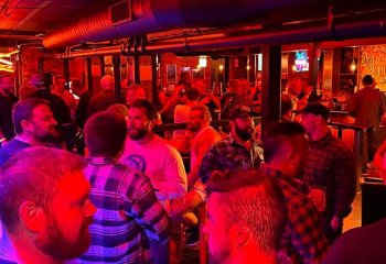 Chicago's Jackhammer gay bar party scene. A lively crowd of men in a dimly lit, industrial-chic space. Red and blue lights add to the ambiance.