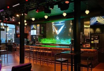 Interior of Jackhammer gay bar in Chicago. Bar stools line the counter, illuminated by colorful lights, creating a party atmosphere.