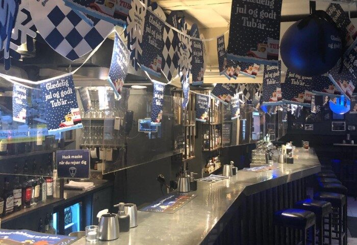 Jailhouse CPH Copenhagen: Interior of a gay bar decorated for Christmas with Tuborg beer banners. Bar stools line the counter in this gay travel spot.