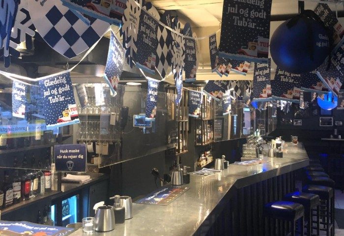 Jailhouse CPH Copenhagen: Interior of a gay bar decorated for Christmas with Tuborg beer banners. Bar stools line the counter in this gay travel spot.