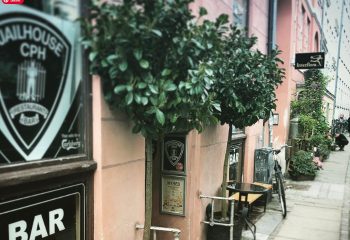 Jailhouse CPH bar in Copenhagen. A pink building with trees, tables, and a bicycle outside. Gay travel in Copenhagen, Denmark.