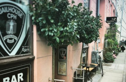 Jailhouse CPH bar in Copenhagen. A pink building with trees, tables, and a bicycle outside. Gay travel in Copenhagen, Denmark.
