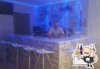 Jimmy's Bar, Benidorm. Bartender at gay bar with blue lights, bottles, and white stools. Gay travel advice for Benidorm's gay scene.