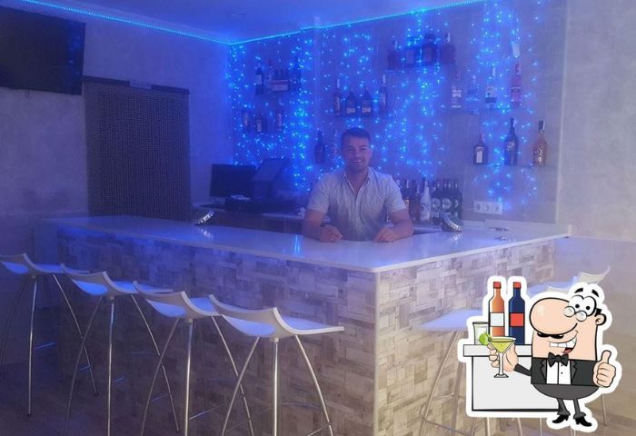 Jimmy's Bar, Benidorm. Bartender at gay bar with blue lights, bottles, and white stools. Gay travel advice for Benidorm's gay scene.