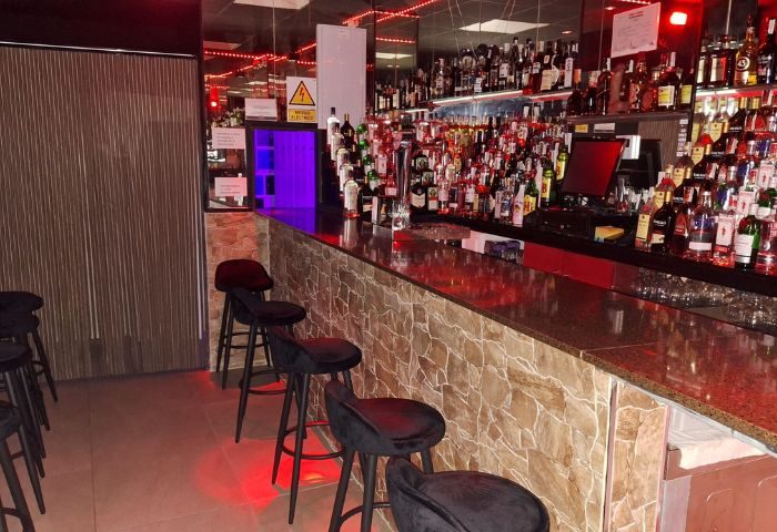 Jimmy's Bar, a gay bar in Benidorm. Stools line the bar, stocked with bottles. Mirrors and red lights give a vibrant atmosphere.