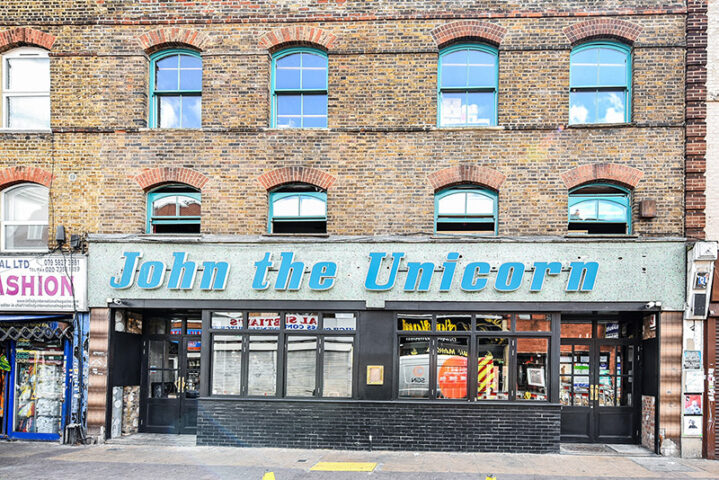 John The Unicorn Gay Bar: A brick building with blue window frames and a sign reading John the Unicorn in blue letters. Gay travel advice.