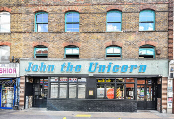John The Unicorn Gay Bar: A brick building with blue window frames and a sign reading John the Unicorn in blue letters. Gay travel advice.