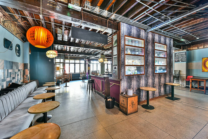 Interior of John The Unicorn gay bar. Lounge seating, bar with stools, and tables. Exposed ceiling and industrial design. Gay travel.