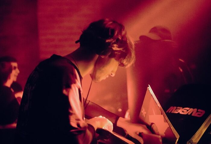 DJ at Jolene Bar, Copenhagen. Red light bathes a man with headphones as he mixes music. Gay nightlife travel destination.
