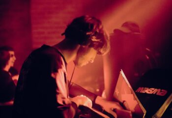 DJ at Jolene Bar, Copenhagen. Red light bathes a man with headphones as he mixes music. Gay nightlife travel destination.