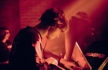 DJ at Jolene Bar, Copenhagen. Red light bathes a man with headphones as he mixes music. Gay nightlife travel destination.