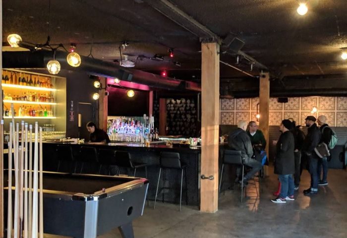 Interior of Jolene's Queer Bar in San Francisco. Pool table, bar with patrons, and shelves of liquor. Gay travel advice.