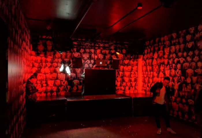Interior of Jolene's Queer Bar in San Francisco, a gay travel destination. Red lighting, stage, and wallpaper with torso images.