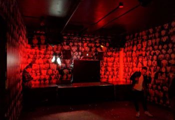Interior of Jolene's Queer Bar in San Francisco, a gay travel destination. Red lighting, stage, and wallpaper with torso images.
