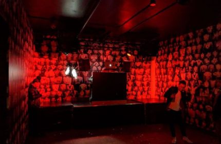 Interior of Jolene's Queer Bar in San Francisco, a gay travel destination. Red lighting, stage, and wallpaper with torso images.