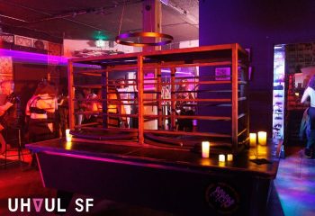 Interior of Jolene's Queer Bar in San Francisco. Dark atmosphere with a cage-like structure, candles, and patrons. Gay travel nightlife scene.