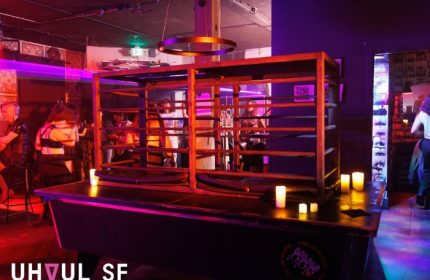 Interior of Jolene's Queer Bar in San Francisco. Dark atmosphere with a cage-like structure, candles, and patrons. Gay travel nightlife scene.