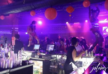 Jolene's Queer Bar in San Francisco: Performers dance above the bar in a crowded, purple-lit space with orange lanterns. Gay nightlife.