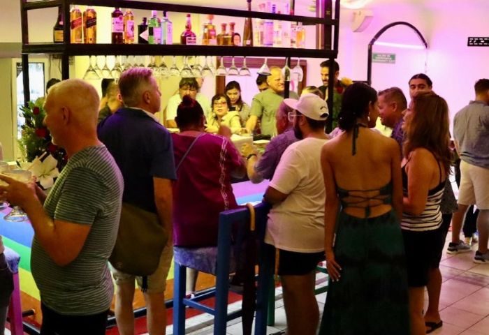 Kevin's Hideaway gay bar in Puerto Vallarta, Mexico. Patrons at the bar, bottles on shelves, and rainbow colors. Gay travel.