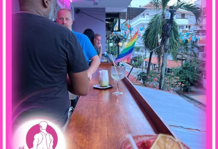 Kevin's Hideaway gay bar in Puerto Vallarta. Men at the bar with tropical drinks, rainbow flag, and a view of the city.
