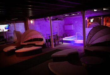 Key West Sauna Paris: Relaxing space with lounge chairs, a bench, and a pool, illuminated with purple lights. Gay travel destination.