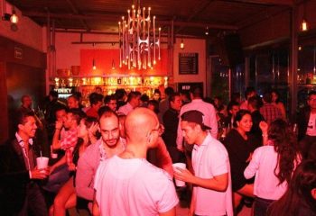 Inside Kinky Bar, a gay bar in Mexico, patrons enjoy drinks. The scene is lively with people socializing under warm, red lighting.