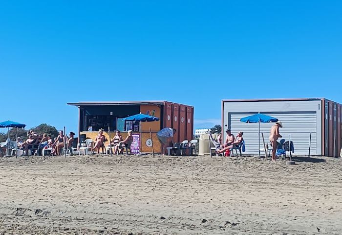 Gran Canaria gay bar kiosk on beach. Patrons relax under umbrellas. Gay travel destination, Maspalomas beach scene.