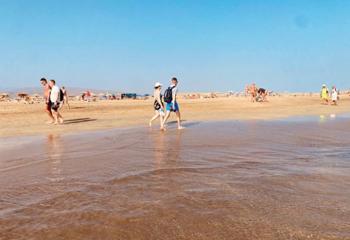 Gran Canaria beach scene. People walking on the beach near a gay bar kiosk. Blue sky, golden sand, and shallow water. Gay travel.