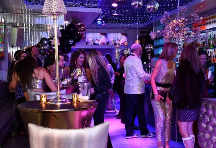 Kit Kat Lounge Supper Club gay party in Chicago. People socializing at a crowded, upscale bar with disco balls and purple lighting.