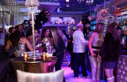Kit Kat Lounge Supper Club gay party in Chicago. People socializing at a crowded, upscale bar with disco balls and purple lighting.