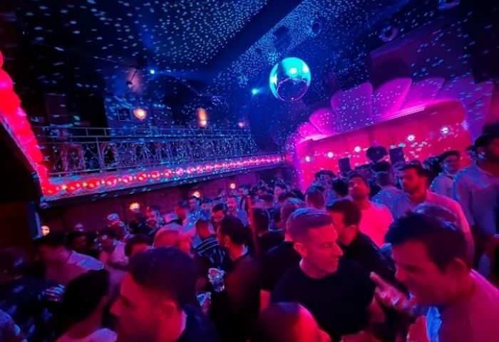 Crowded Kluster gay club in Madrid. Men dancing under disco ball and pink lights. Gay nightlife travel destination.