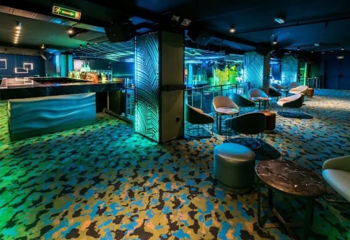Interior of Kluster, a gay club in Madrid. Lounge area with bar, chairs, and tables. Blue and green lighting. Gay travel.