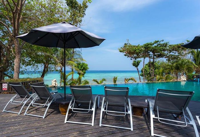 Phi Phi Holiday Resort pool view. Beachfront hotel with lounge chairs, umbrella, and ocean. Gay-friendly travel destination.