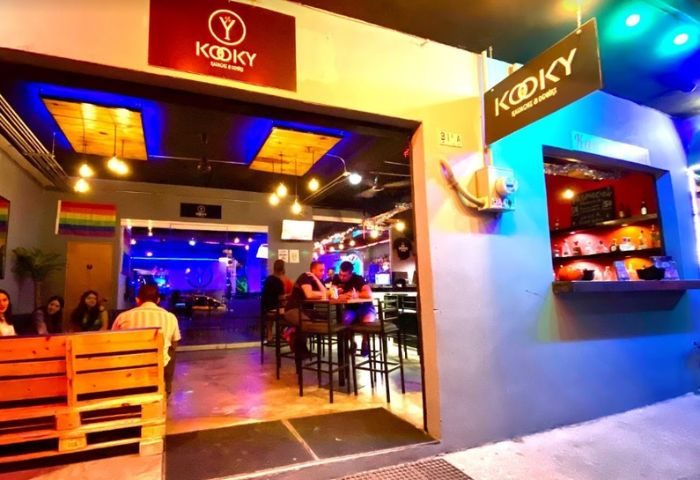 Kooky Karaoke in Puerto Vallarta's gay scene. Patrons enjoy drinks at the bar in a vibrant, colorful setting with rainbow flag.