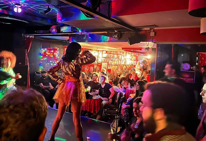 Koukles Club Athens: Drag show performance. Audience watching drag queens on stage in a crowded gay bar. Nightlife and gay travel in Athens.