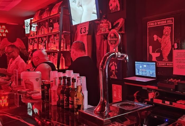Inside Kuma Bar, Benidorm gay bar, featuring drinks, patrons, and red lighting. A popular party spot in Benidorm for gay men.